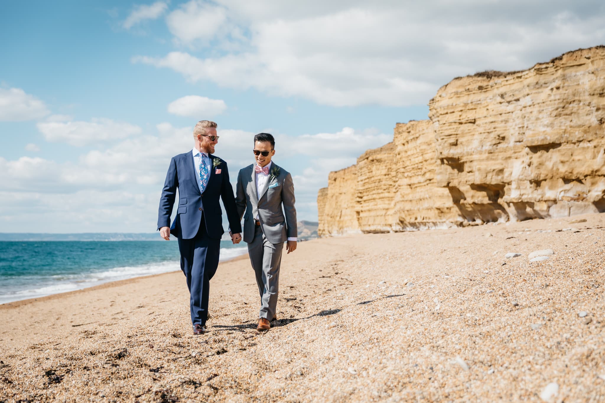Same sex couple walking along the beach to their wedding